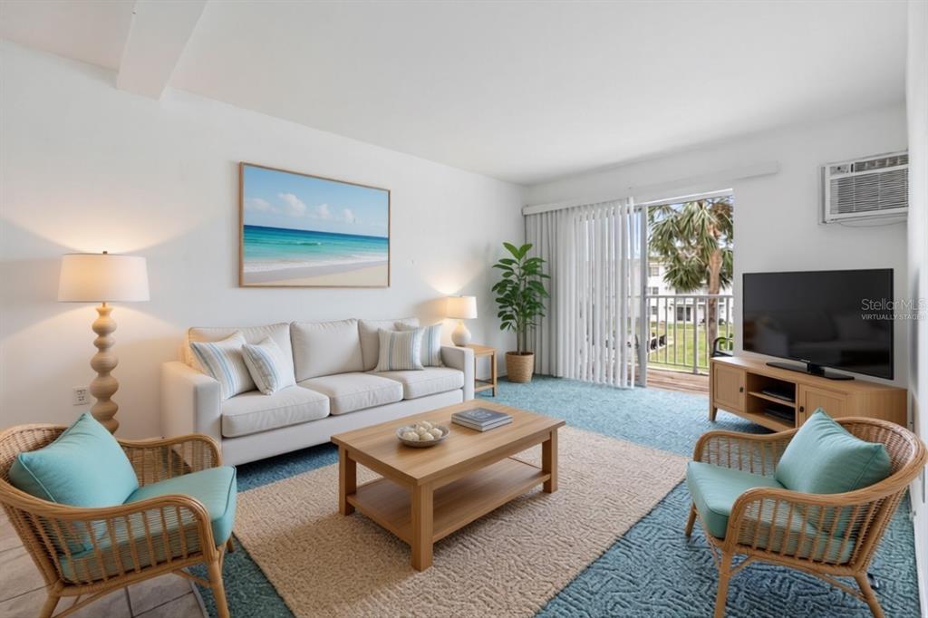 A balcony with a teal chair overlooks a grassy courtyard with a pool and tennis court — 2326 CANAL DRIVE UNIT G25, BRADENTON, FL