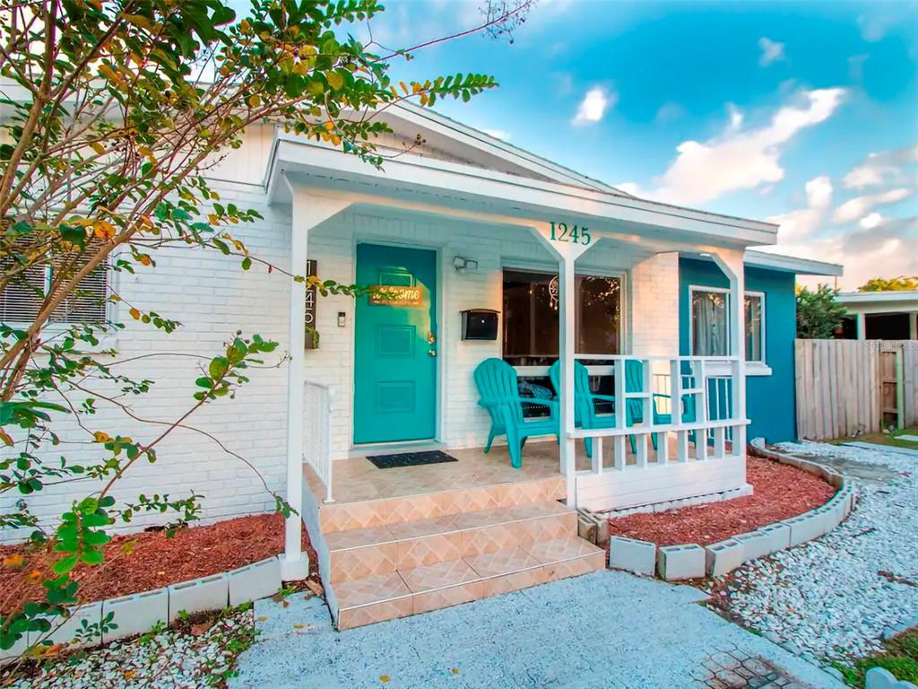 A white brick house features a teal front door and a small covered porch with chairs — 1245 CATALPA LANE, ORLANDO, FL