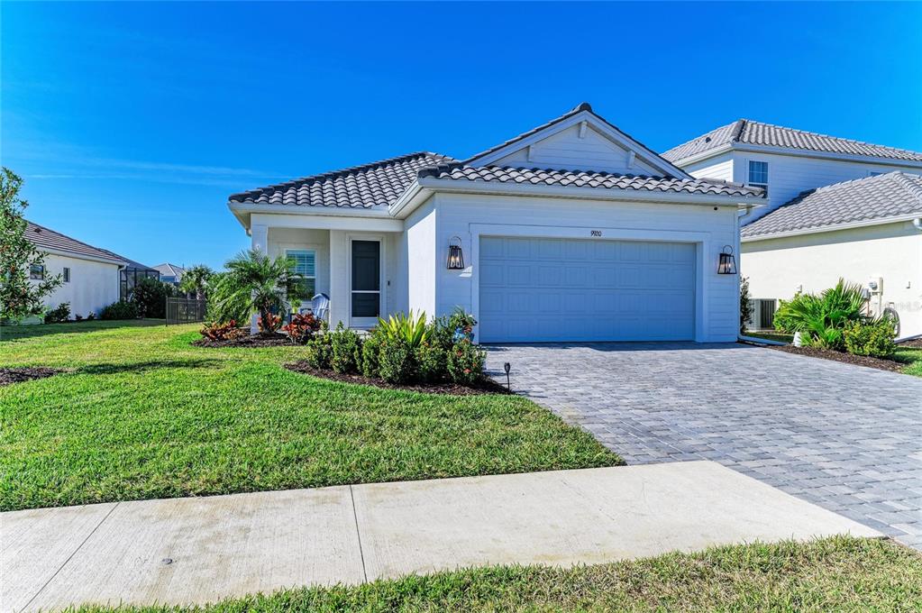 A single-story house with a white exterior, a tiled roof, and a paved driveway — 9920 CRYSTAL ISLE CIRCLE, SARASOTA, FL