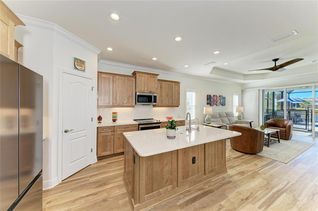 A kitchen with light wood cabinets and a white island opens into a living area — 9920 CRYSTAL ISLE CIRCLE, SARASOTA, FL