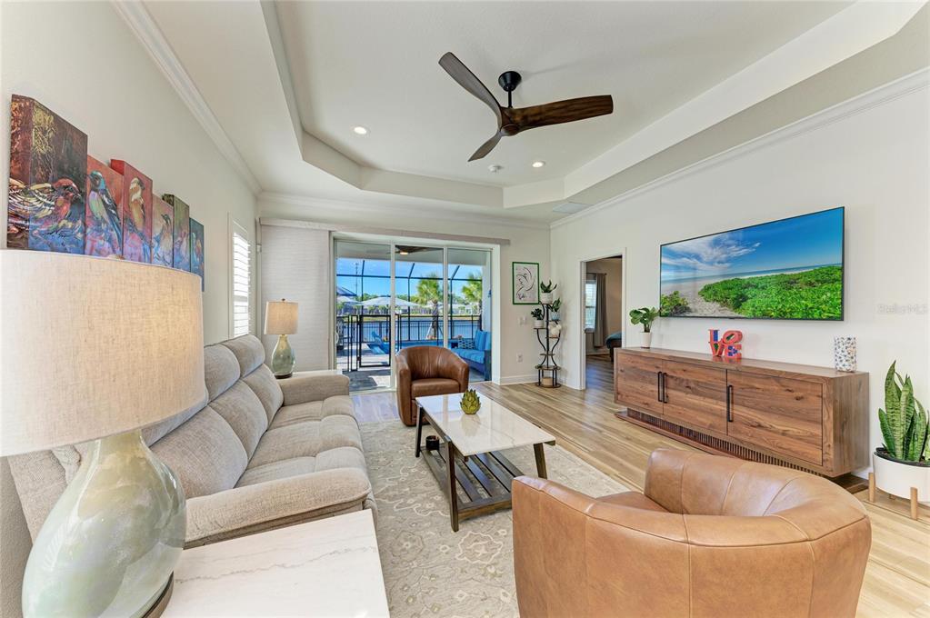 A living room features a tray ceiling, leather armchairs, a sofa, and a sliding glass door — 9920 CRYSTAL ISLE CIRCLE, SARASOTA, FL