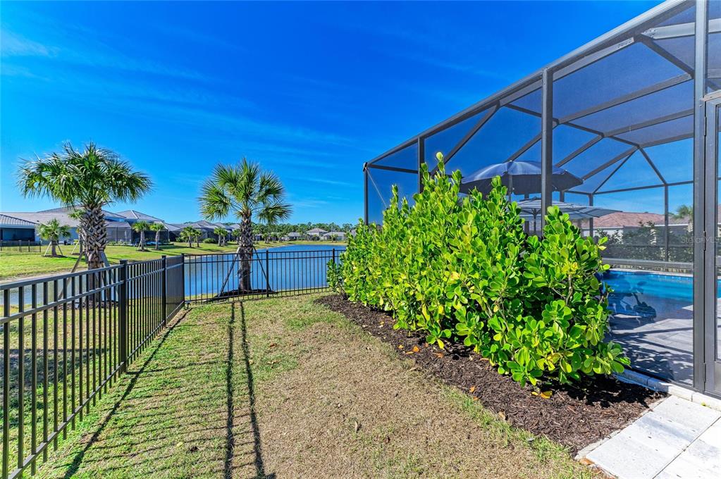 A fenced backyard with a pool enclosure, landscaping, and a view of a pond — 9920 CRYSTAL ISLE CIRCLE, SARASOTA, FL