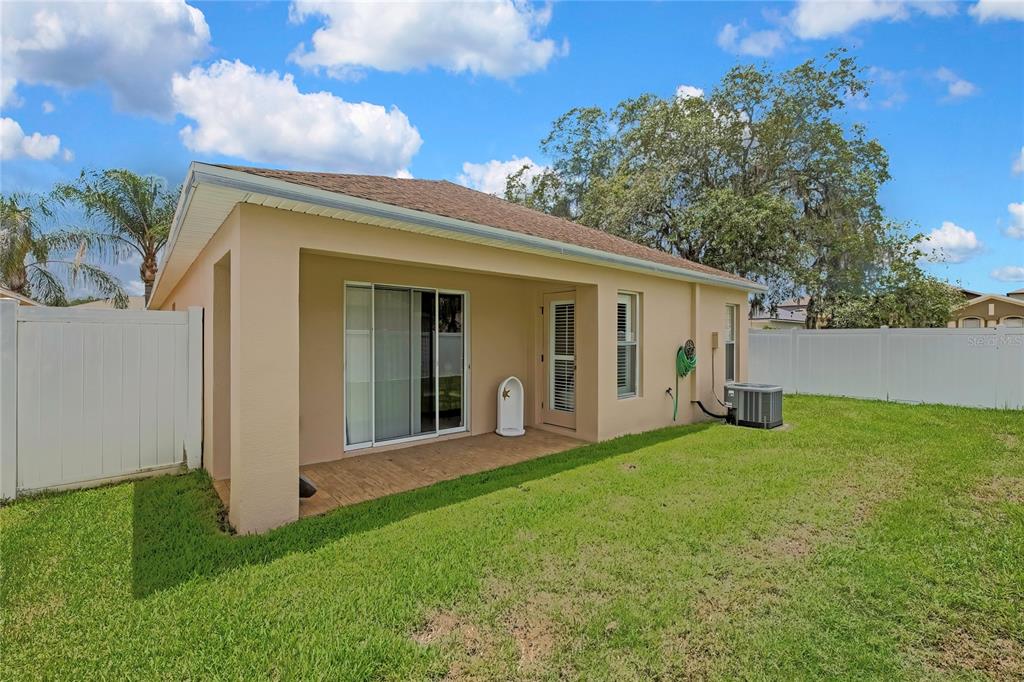 The exterior of a tan house features a covered patio, sliding glass doors, and lawn — 209 WINTHROP DRIVE, SPRING HILL, FL