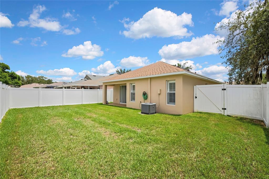 A backyard with a tan house, a white vinyl fence, and a central air unit — 209 WINTHROP DRIVE, SPRING HILL, FL