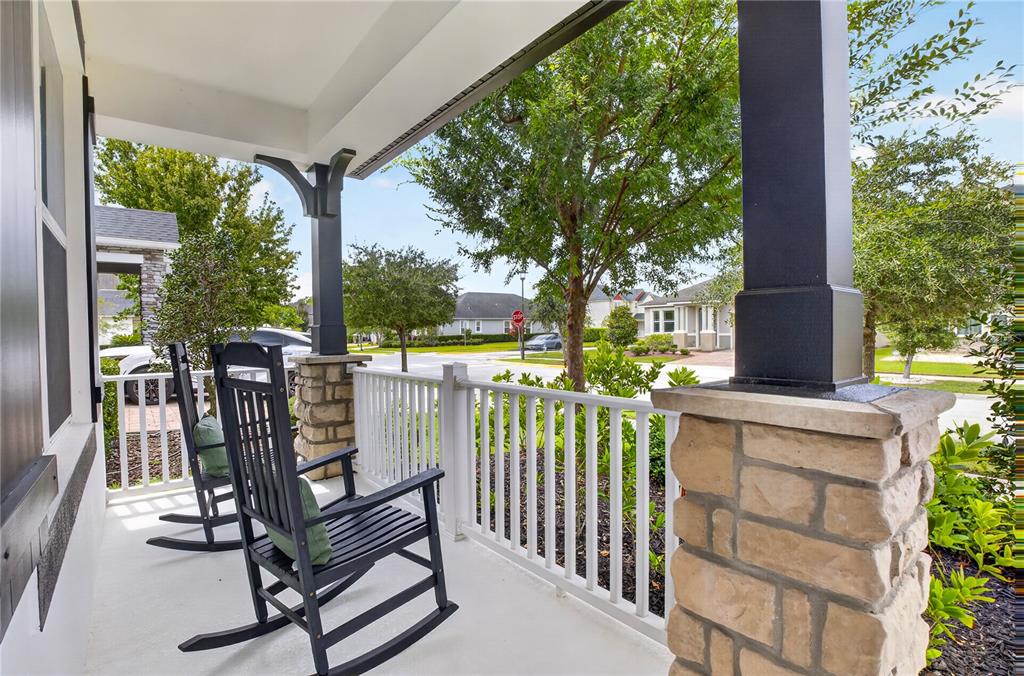 A covered front porch features two black rocking chairs, white railings, and stone-based pillars — 8163 CORKFIELD AVENUE, ORLANDO, FL