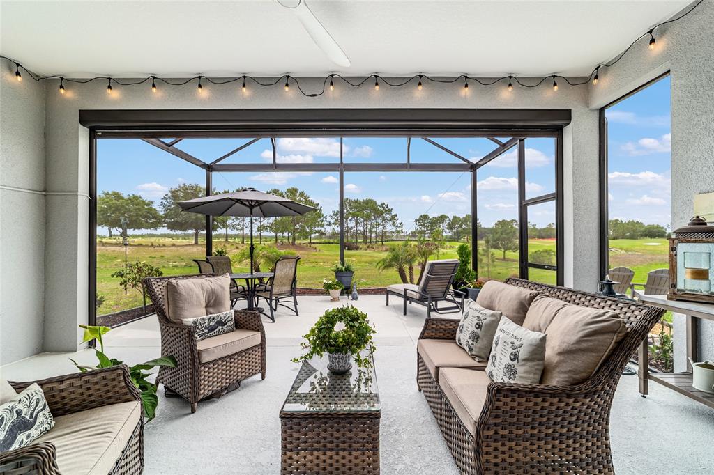 A covered patio with wicker furniture overlooks a grassy golf course through a screened enclosure — 8606 SW 61ST LOOP, OCALA, FL