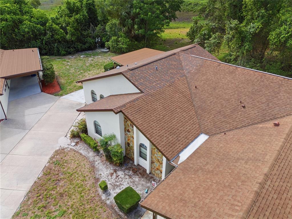 An aerial view shows a house with a brown shingled roof, stone facade, and driveway — 9199 LINGROVE ROAD, WEEKI WACHEE, FL