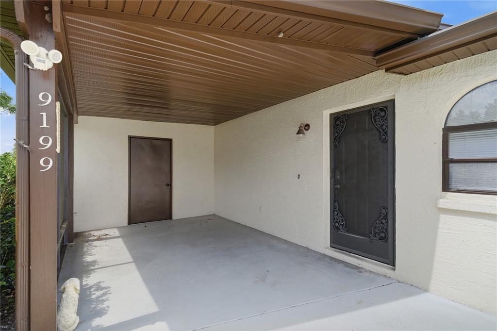 A covered concrete porch features a brown door, a screen door, and house numbers — 9199 LINGROVE ROAD, WEEKI WACHEE, FL