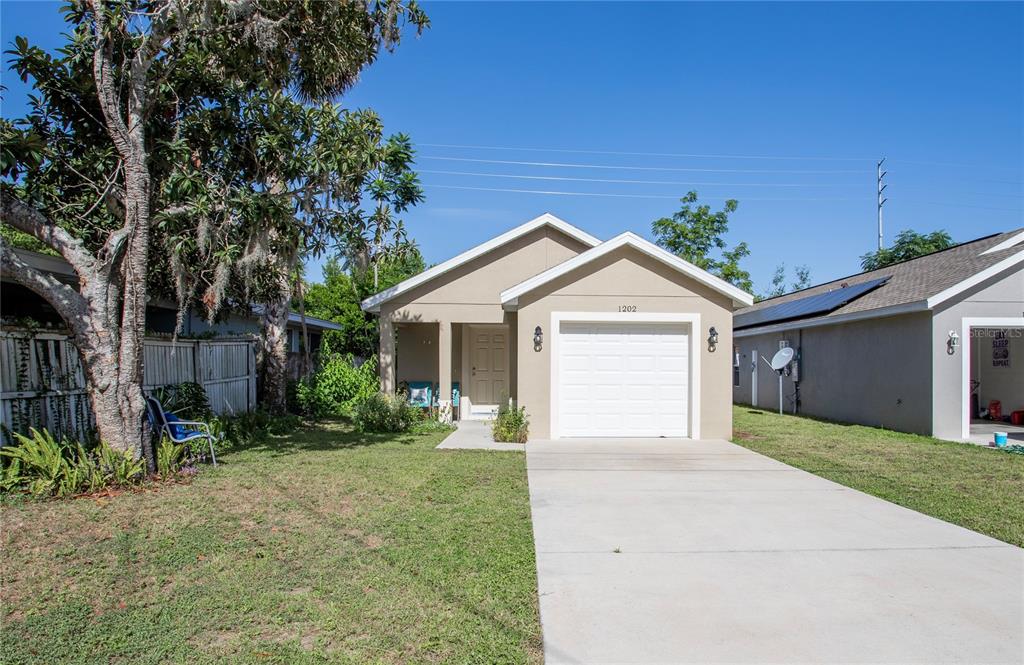 A single-story house with a beige exterior, a white garage door, and a concrete driveway — 1202 S DEWEY STREET, EUSTIS, FL