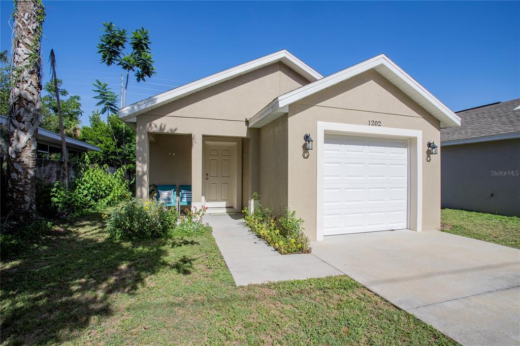 A single-story house with a beige stucco exterior, a white garage door, and a front porch — 1202 S DEWEY STREET, EUSTIS, FL