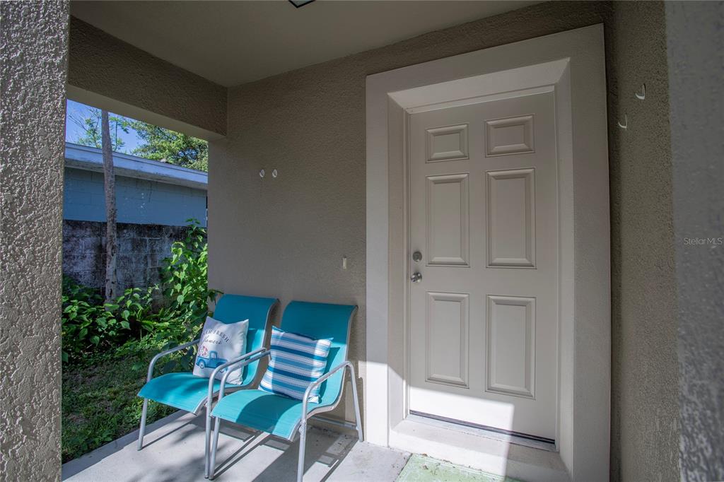 A covered entryway features a white door and two turquoise chairs on a concrete porch — 1202 S DEWEY STREET, EUSTIS, FL