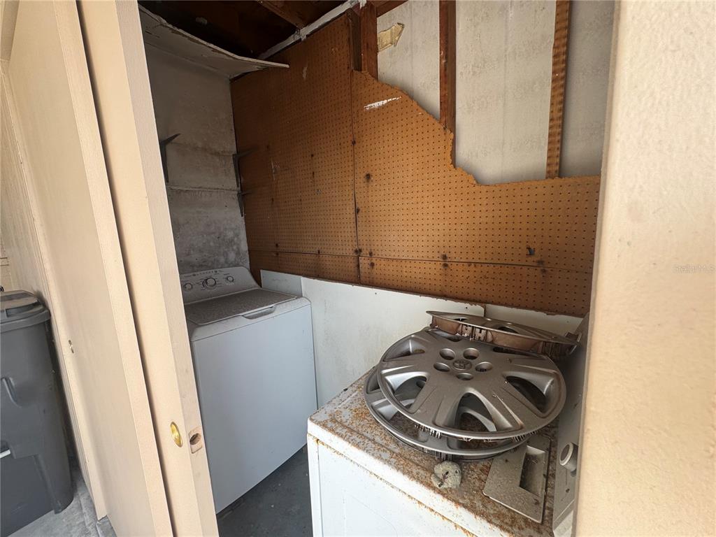 A laundry area features a washing machine, a dryer with hubcaps, and damaged pegboard walls — 652 PARK CIRCLE, BRADENTON, FL