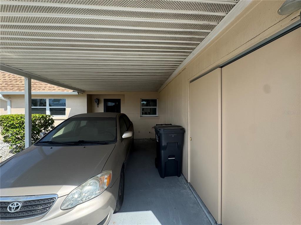 A beige house exterior features a covered carport with a parked car and storage closet — 652 PARK CIRCLE, BRADENTON, FL