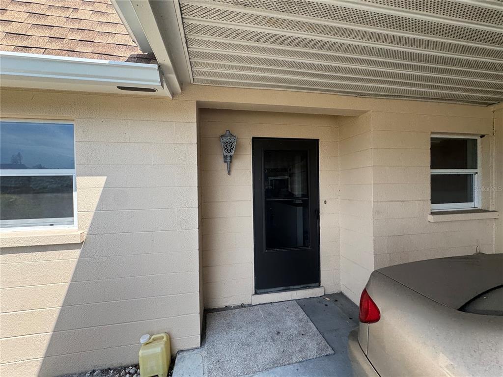 A beige concrete block house exterior features a dark storm door and a covered carport — 652 PARK CIRCLE, BRADENTON, FL