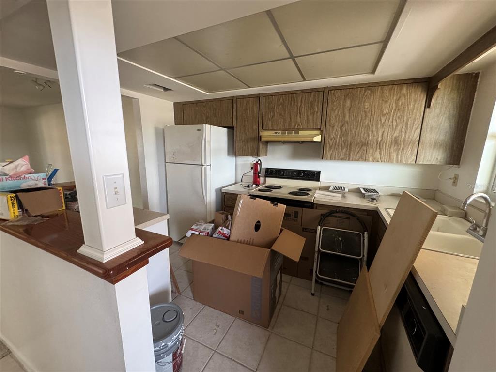 A kitchen features wood-grain cabinets, a white refrigerator, a drop-in stove, and tiled flooring — 652 PARK CIRCLE, BRADENTON, FL