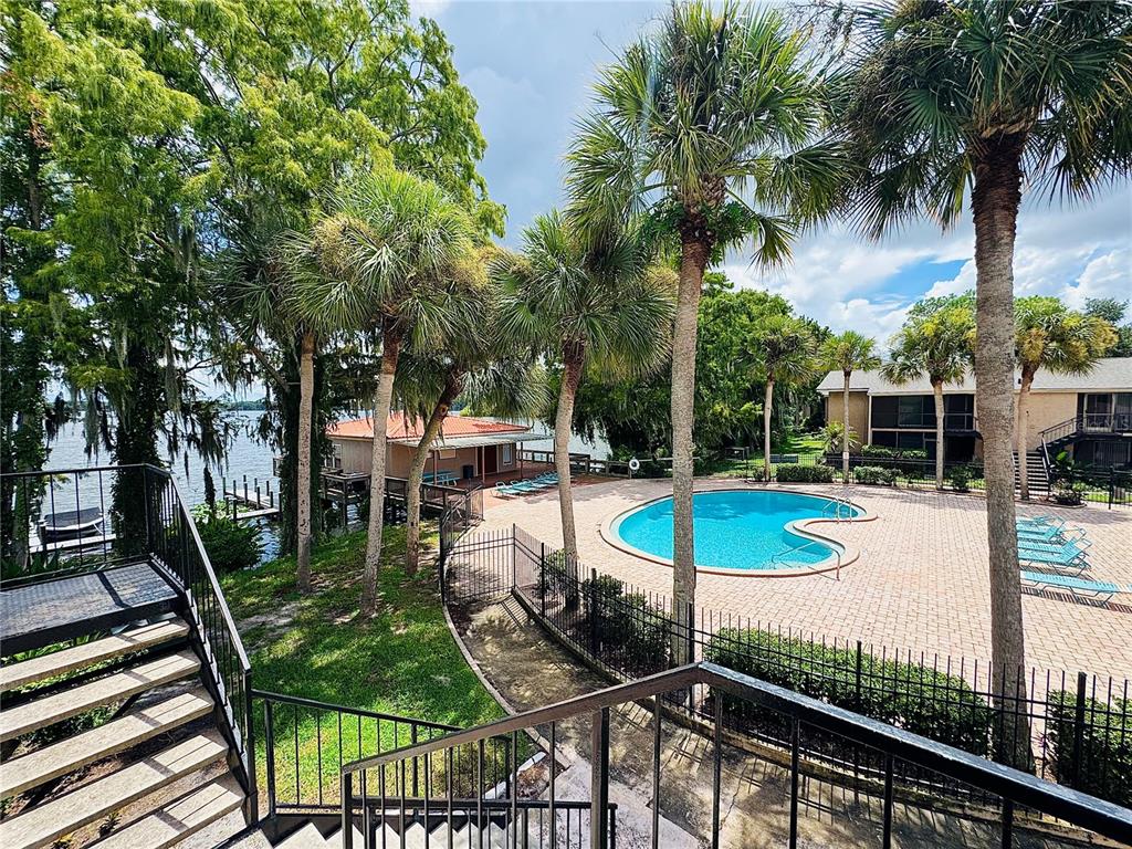 An outdoor swimming pool and a small building are situated near a lake with palm trees — 1180 PASEO DEL MAR UNIT C, CASSELBERRY, FL