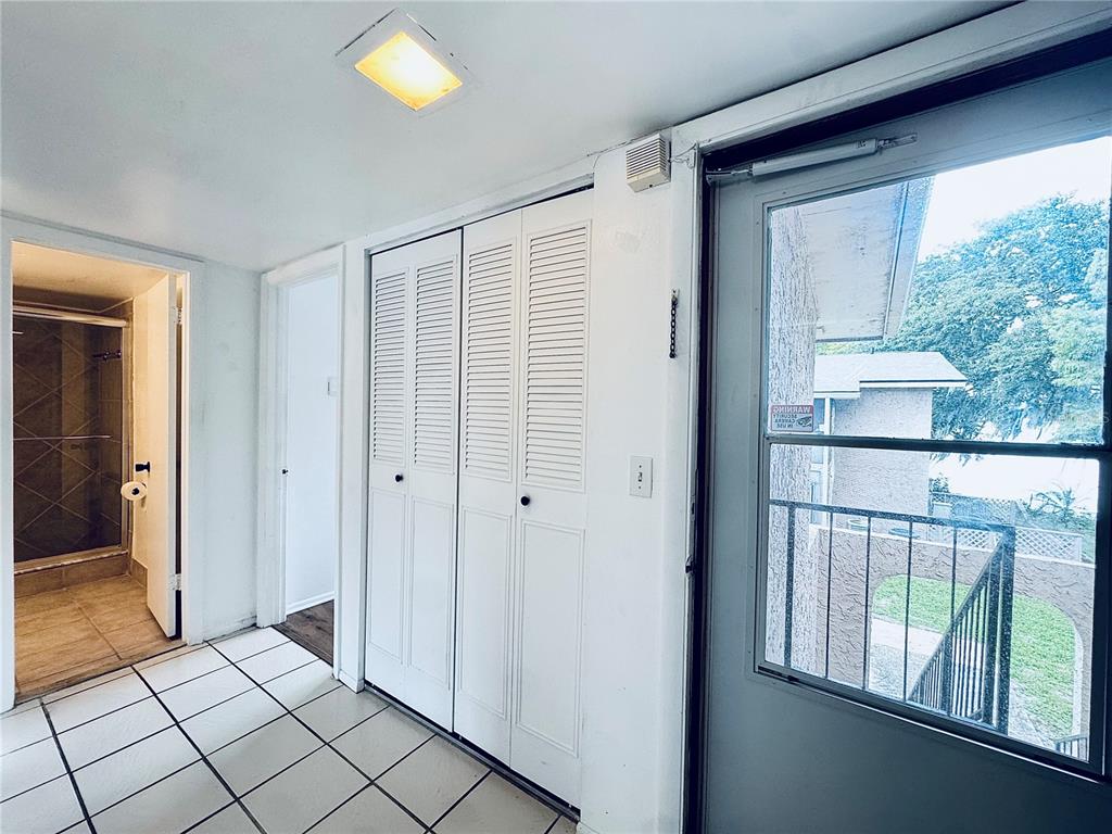 A tiled room features white louvered closet doors, a doorway to a bathroom, and a balcony — 1180 PASEO DEL MAR UNIT C, CASSELBERRY, FL