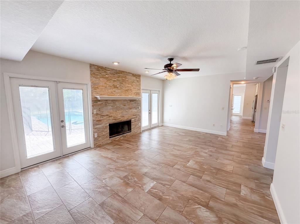 A living room features a stone fireplace, tile flooring, a ceiling fan, and glass doors — 120 LONGBRANCH ROAD, WINTER PARK, FL