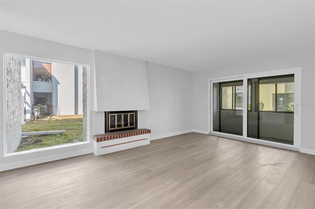 A living room features light wood-look flooring, a white fireplace, and large windows and doors — 1 WINDRUSH BOULEVARD UNIT 87, INDIAN ROCKS BEACH, FL