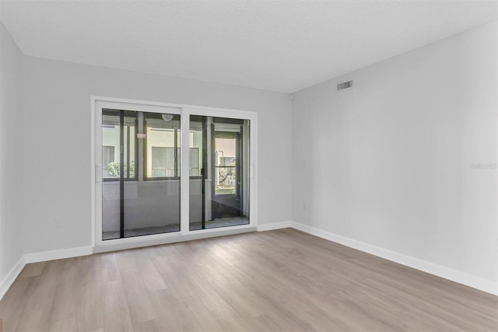 An empty room with light wood-look flooring and sliding glass doors leading to a balcony — 1 WINDRUSH BOULEVARD UNIT 87, INDIAN ROCKS BEACH, FL