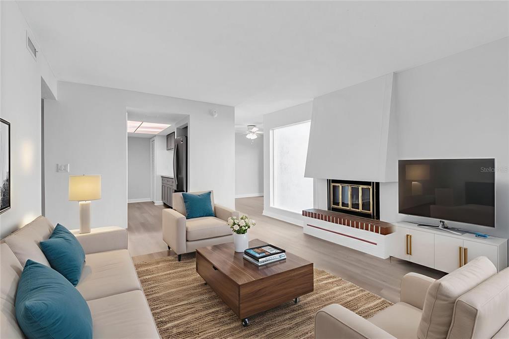 A living room features a fireplace, a television, light wood floors, and neutral-toned furniture — 1 WINDRUSH BOULEVARD UNIT 87, INDIAN ROCKS BEACH, FL
