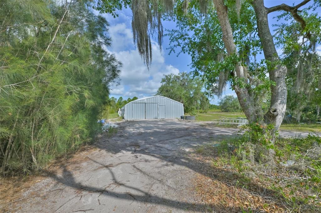 A yellow single-story house sits behind a chain-link fence and a wooden overhead gate — 14451 HIGHLAND ROAD, WIMAUMA, FL