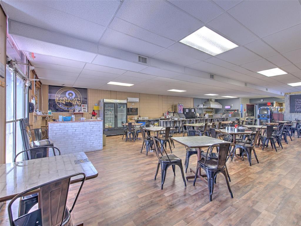 A restaurant interior features wood-look flooring, multiple tables with metal chairs, and a service counter — 8001 S 301 HIGHWAY, RIVERVIEW, FL