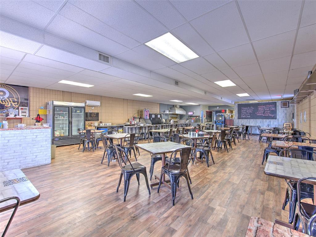 A restaurant dining area features multiple tables, metal chairs, wood-look flooring, and a menu board — 8001 S 301 HIGHWAY, RIVERVIEW, FL