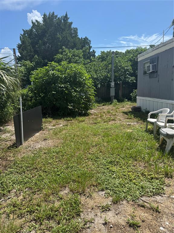 A grassy yard sits beside a mobile home with white plastic chairs on the side — 7417 GULF BREEZE CIRCLE, HUDSON, FL