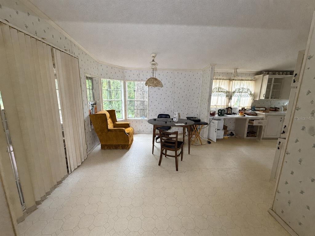 A dining area with patterned wallpaper, a round table, a yellow armchair, and linoleum flooring — 15171 NE 154TH LANE, FORT MC COY, FL