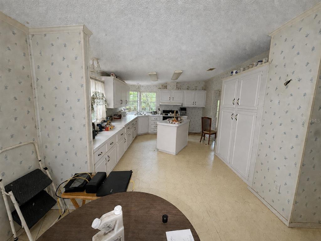 A kitchen with white cabinetry, a center island, patterned wallpaper, and light-colored vinyl flooring — 15171 NE 154TH LANE, FORT MC COY, FL