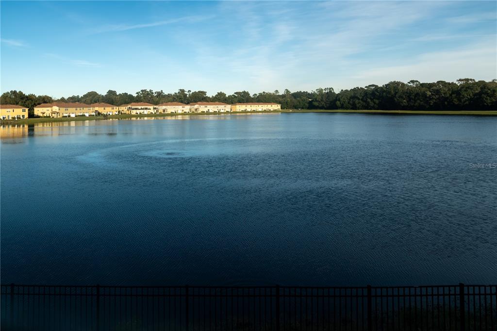 A large lake sits in front of a row of residential townhomes under a blue sky — 3733 EAGLE PRESERVE POINT, SANFORD, FL