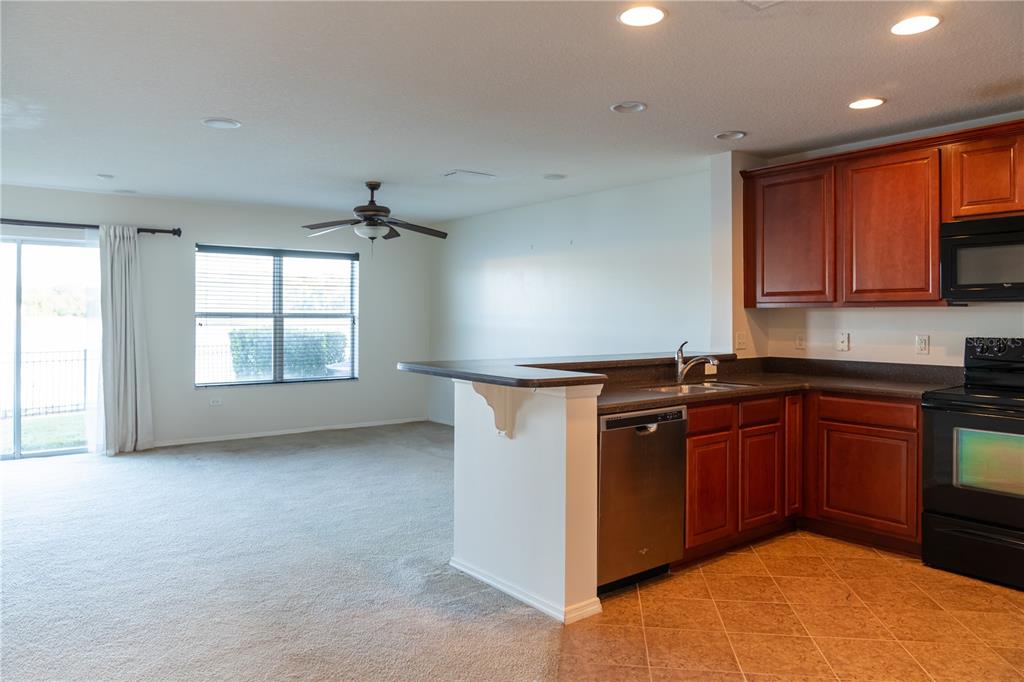 A kitchen with wood cabinets and a dishwasher opens to a carpeted living area — 3733 EAGLE PRESERVE POINT, SANFORD, FL