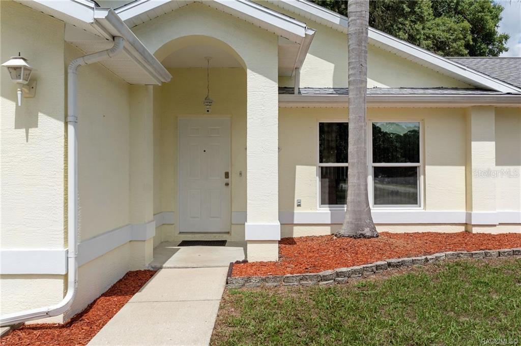 The exterior of a light yellow house features a covered entryway and a palm tree — 1014 STETSON TERRACE, INVERNESS, FL
