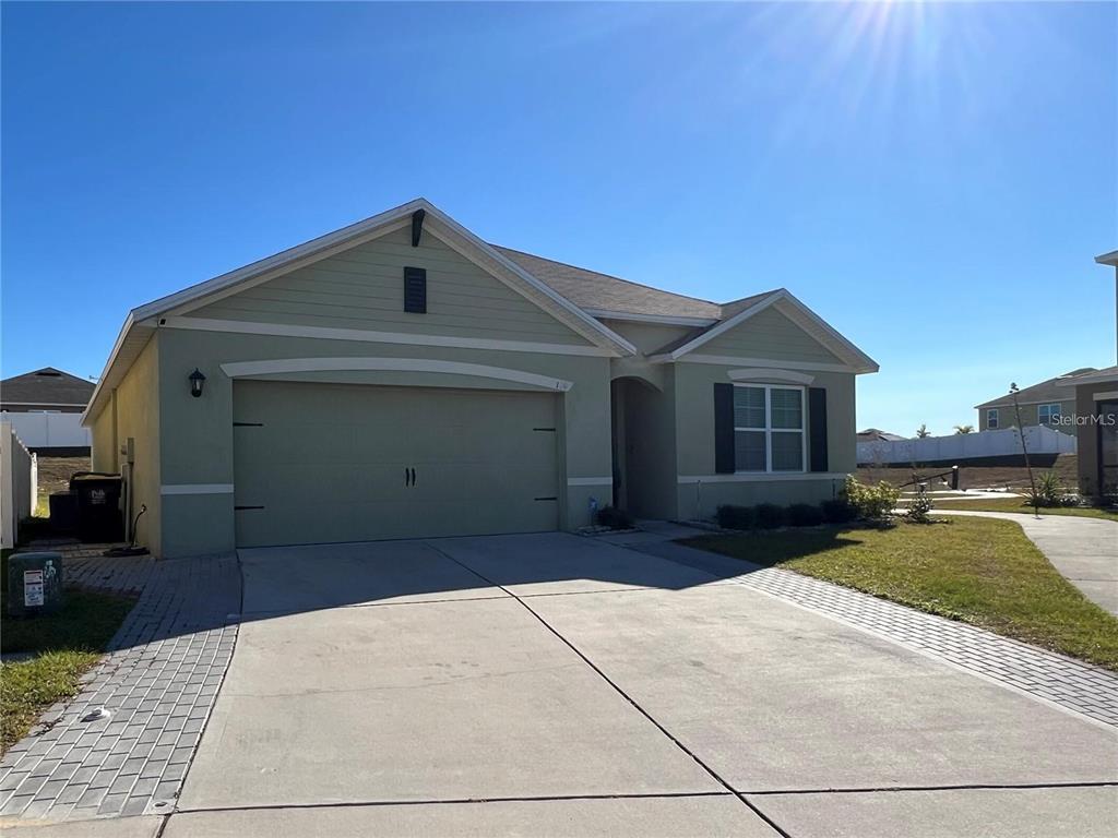 A light green single-story house features a two-car garage and a paved driveway — 120 PANDA WAY, DAVENPORT, FL