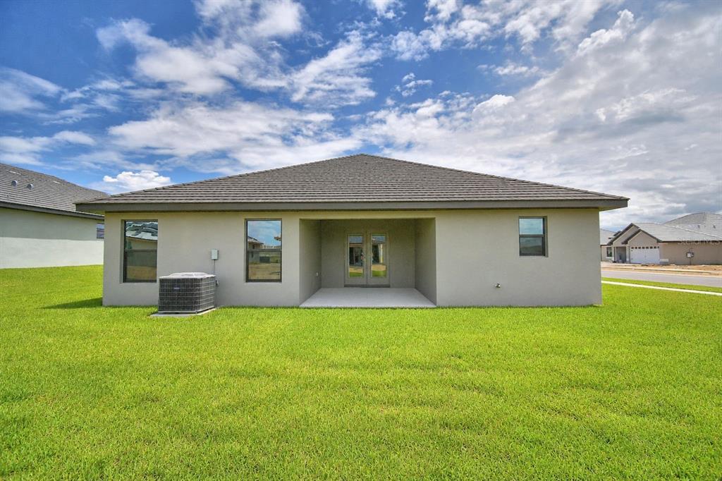 The exterior rear view of a single-story house features a covered patio and lawn — 4616 CALAMINT LANE, AUBURNDALE, FL