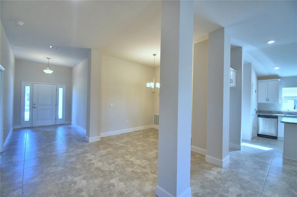 An open-concept interior features a tiled floor, white walls, support columns, and a kitchen area — 4616 CALAMINT LANE, AUBURNDALE, FL