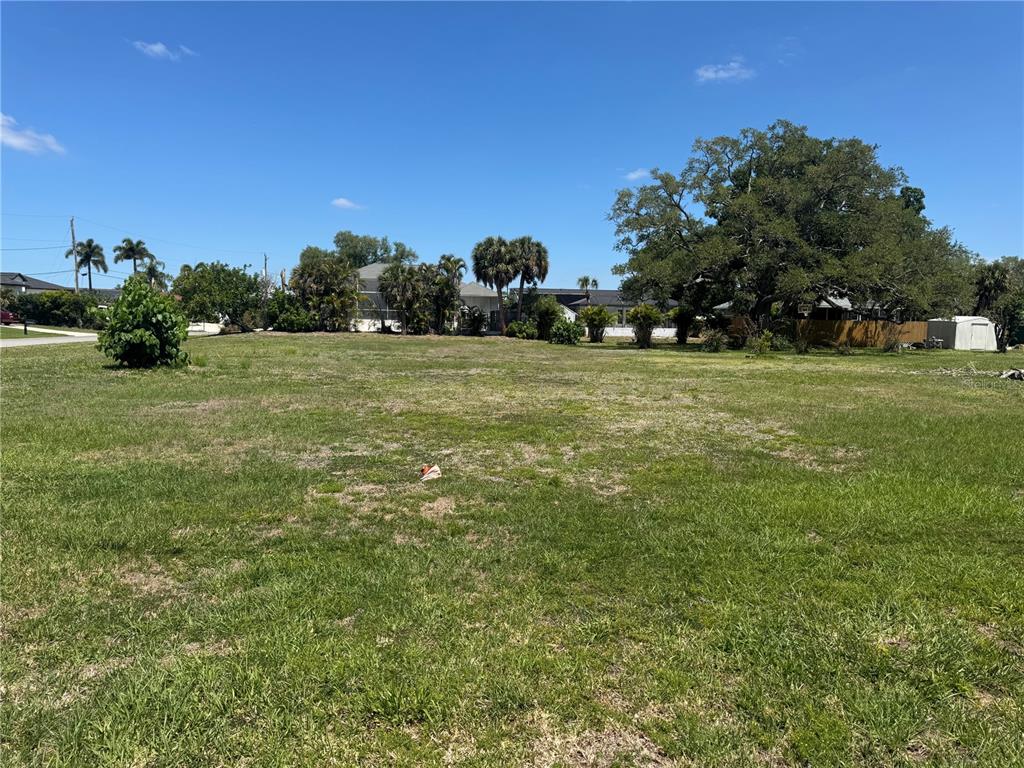 A large, flat, grassy vacant lot with scattered trees and neighboring houses in the background — DONA WAY, NOKOMIS, FL
