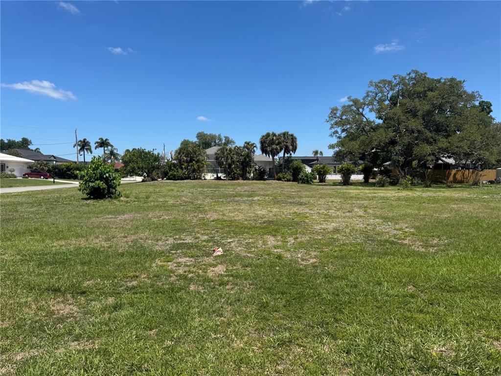 A vacant, grassy residential lot features scattered trees and shrubs under a clear blue sky — DONA WAY, NOKOMIS, FL
