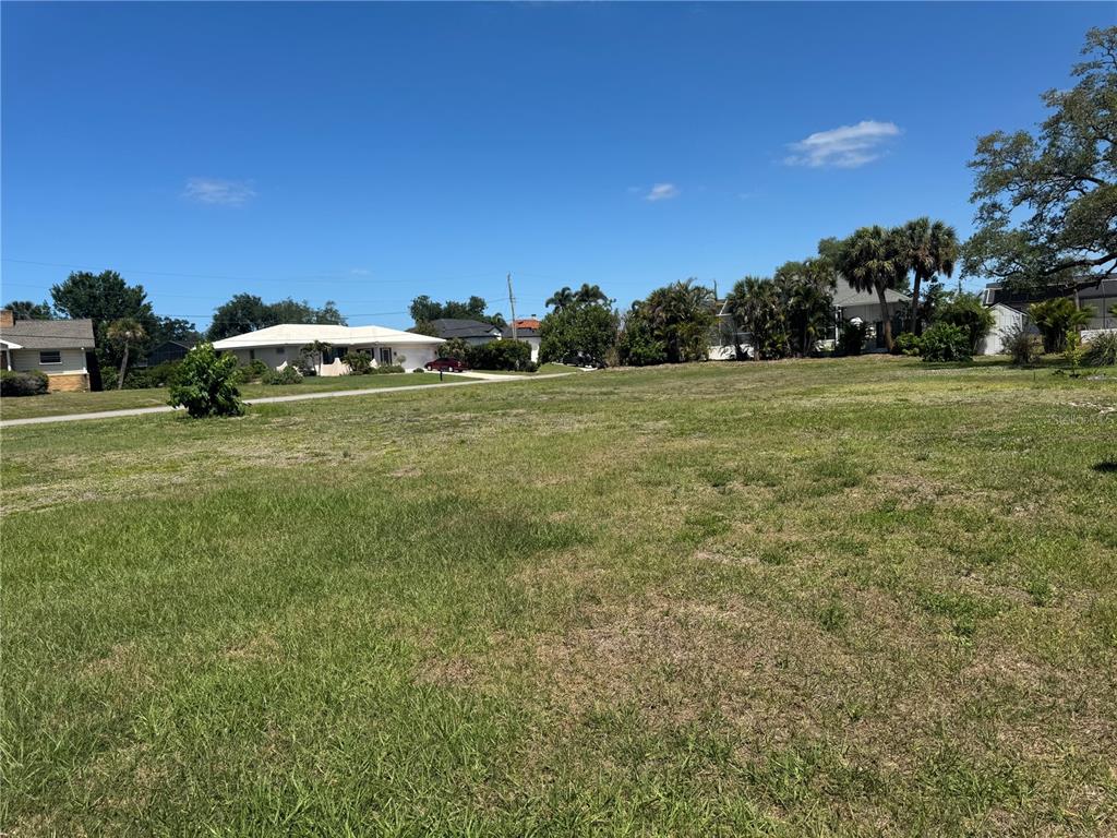 A grassy, vacant residential lot sits under a clear blue sky near neighboring houses — DONA WAY, NOKOMIS, FL