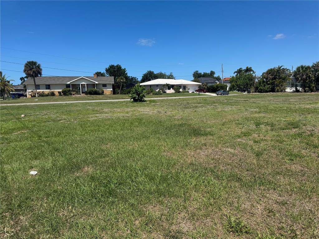 A grassy vacant lot sits in front of a residential street with several houses — DONA WAY, NOKOMIS, FL
