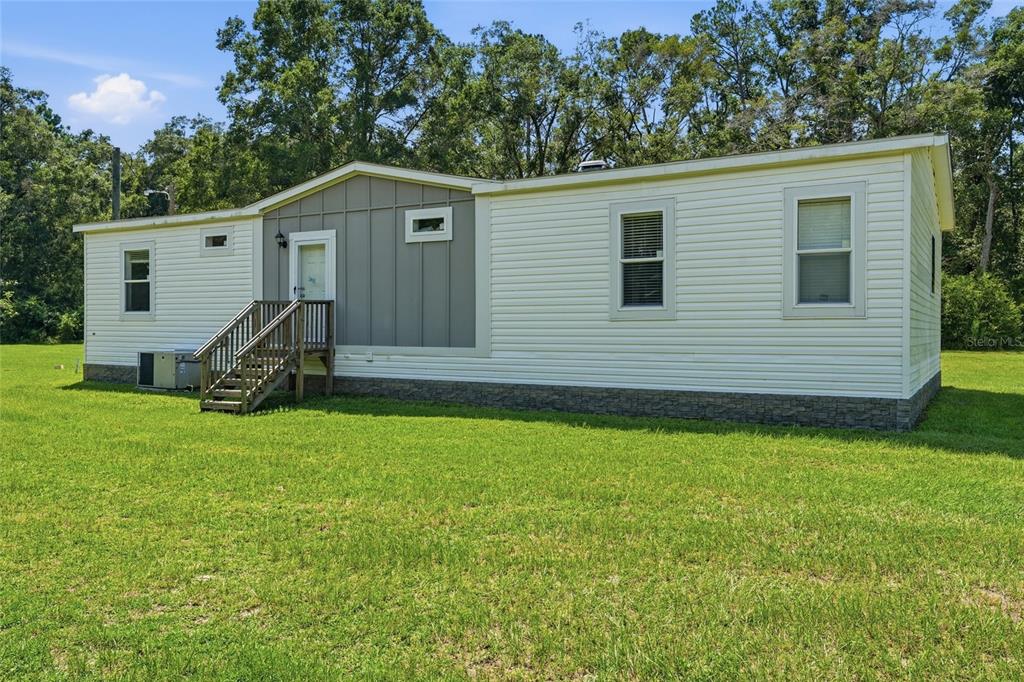 A single-story manufactured home with light siding and a gray accent wall sits on grass — 4754 SW 10TH STREET, BELL, FL