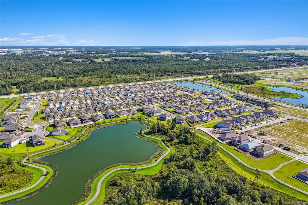 An aerial view shows a suburban neighborhood with houses surrounding a large retention pond — 4997 BASSWOOD STREET, LAKELAND, FL