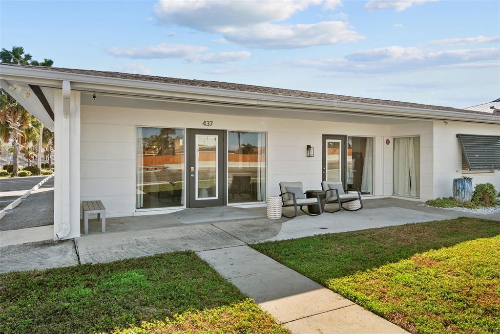 A single-story building exterior features a concrete patio, glass doors, and two rocking chairs — 439 CAUSEWAY BOULEVARD, DUNEDIN, FL
