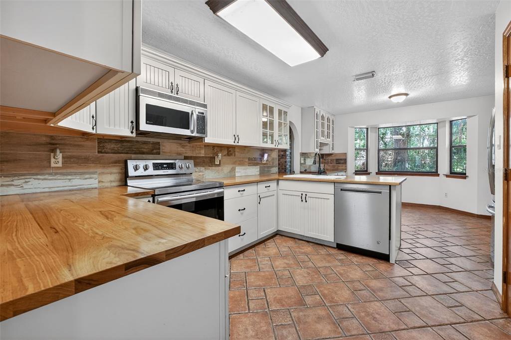 A kitchen with white cabinets, wood countertops, a tile floor, and a stainless steel dishwasher — 3380 LIONEL ROAD, MIMS, FL