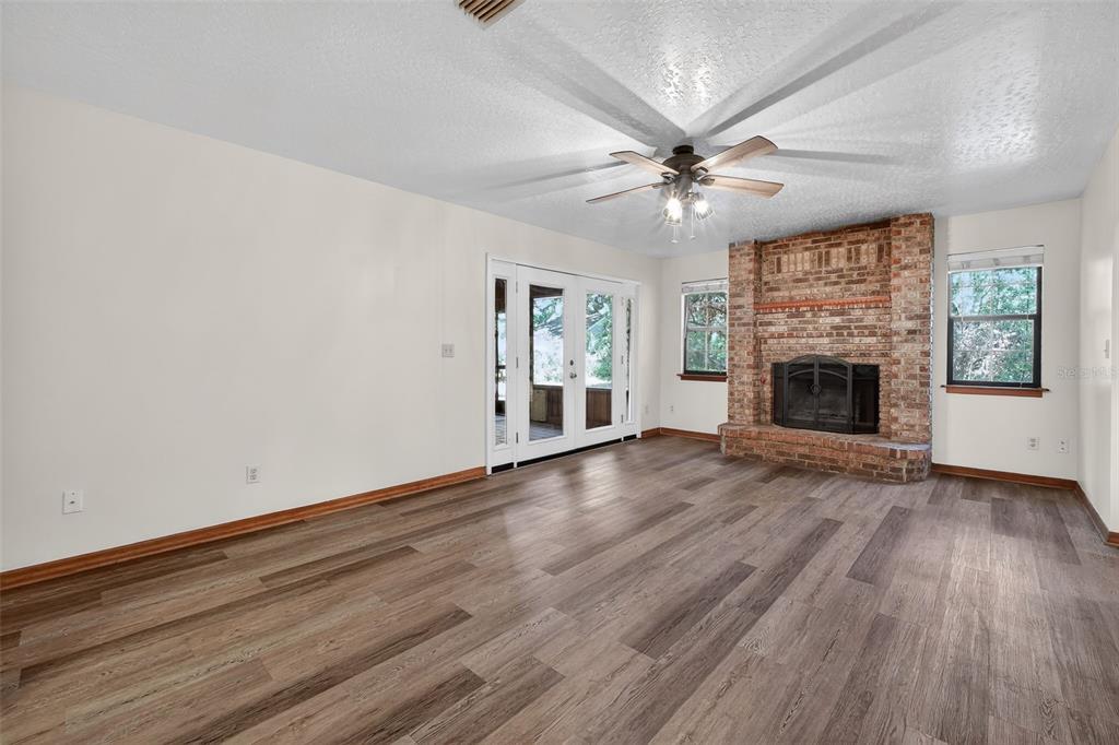 A living room features wood-look flooring, a brick fireplace, and glass doors leading outside — 3380 LIONEL ROAD, MIMS, FL