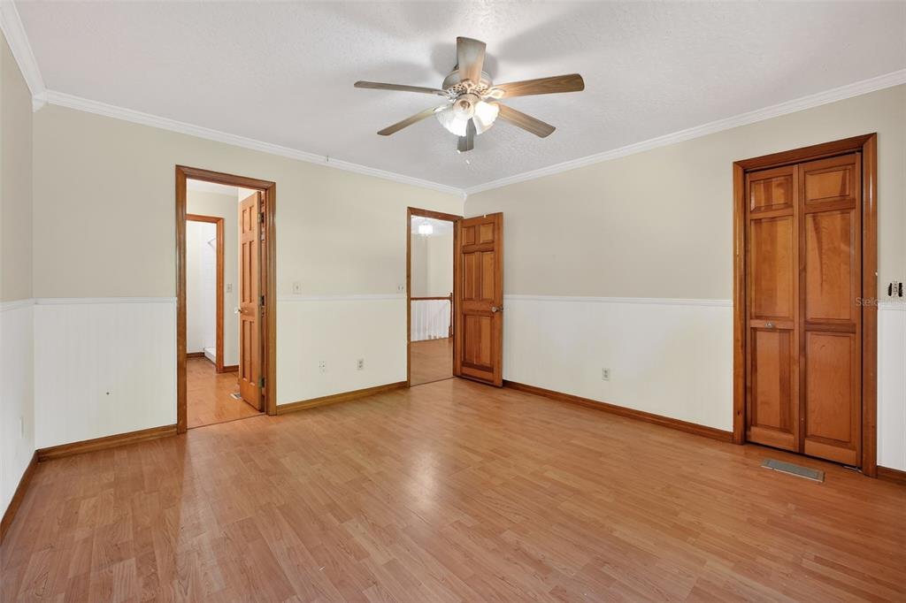 An empty bedroom features hardwood floors, white wainscoting, a ceiling fan, and three wooden doors — 3380 LIONEL ROAD, MIMS, FL
