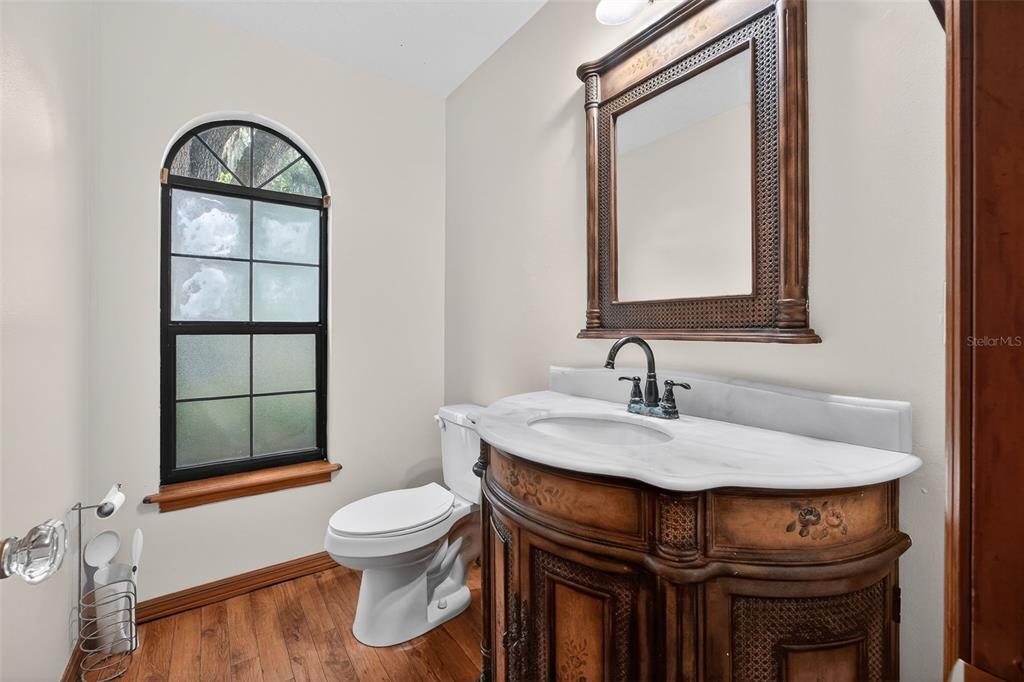 A bathroom features a wood vanity with a marble top, a mirror, and an arched window — 3380 LIONEL ROAD, MIMS, FL