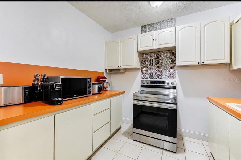 A kitchen features orange countertops, white cabinets, a stainless steel stove, and patterned tile backsplash — 20890 SW 236TH STREET, HOMESTEAD, FL