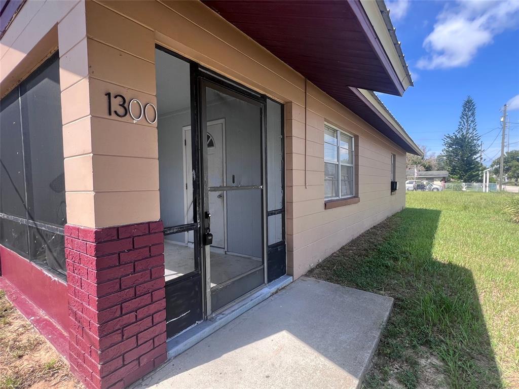 A beige house exterior features a screened-in porch, a brick base, and a house number — 1300 S CAROLINA AVENUE, AVON PARK, FL